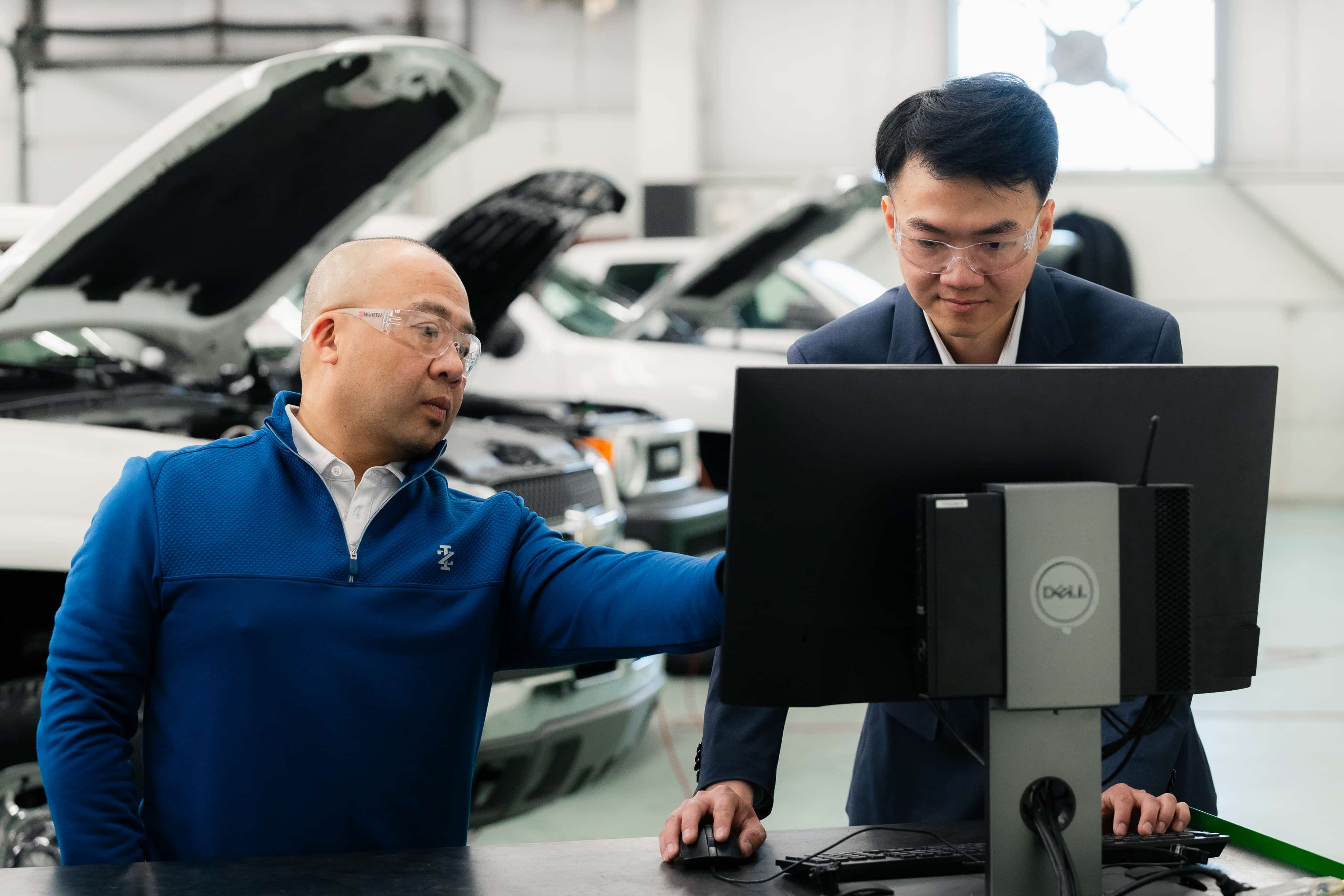 Two men in a car garage look at a computer