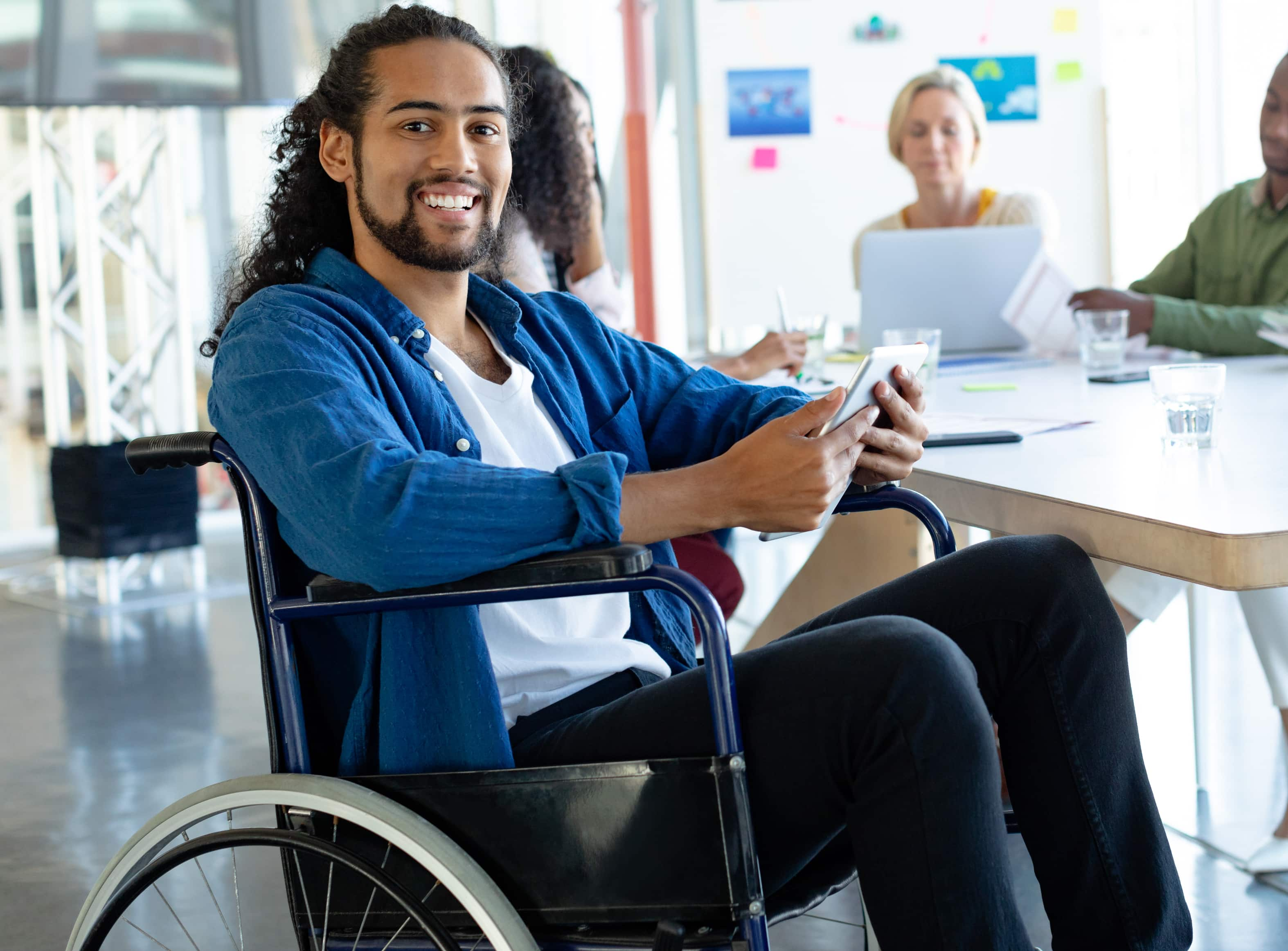 Man in a wheelchair holding a tablet and smiling at camera