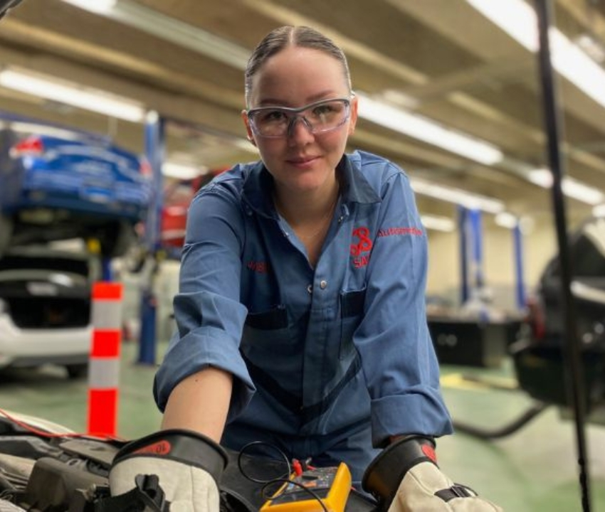 A woman works on the engine of a car