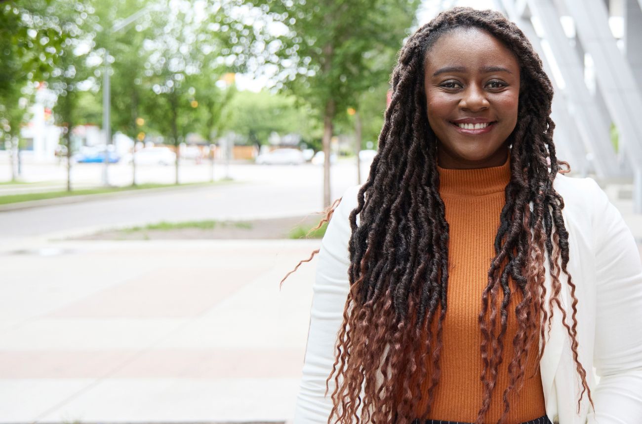 Woman smiling at the camera, outside the Aldred Centre at SAIT in the summer.