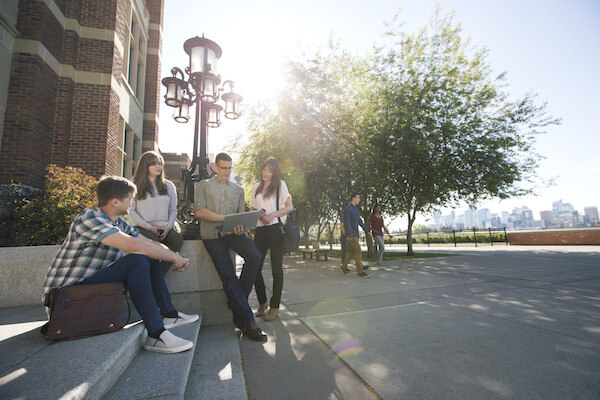 A group of SAIT students look at a computer while sitting outside Heritage Hall.