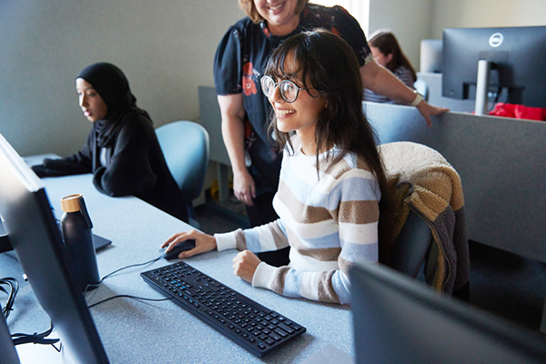 A student looking at a screen while a person stand behind them