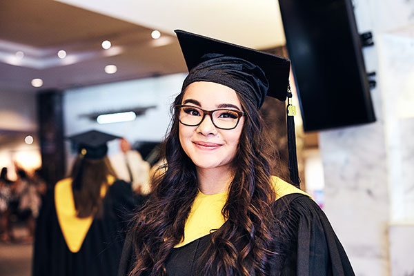 A School of Business graduate wearing her cap and gown smiles.