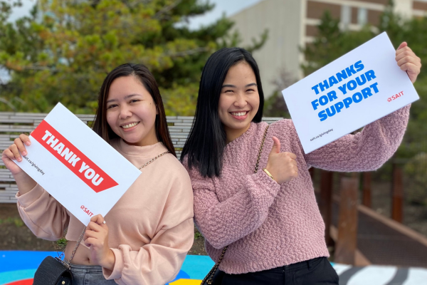 two female students holding up thank you signs