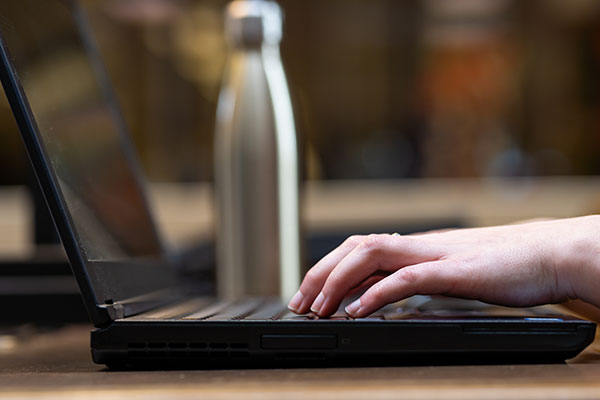 A close-up of fingers on a laptop keyboard. A water bottle is in the background.