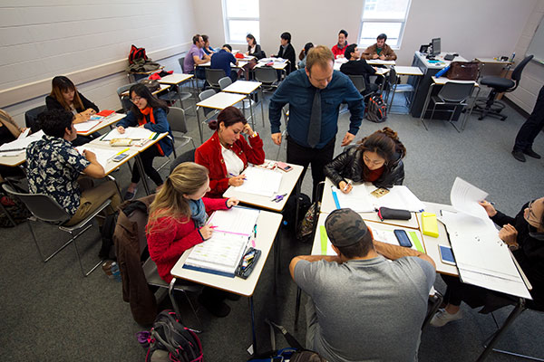 A high-level view of students in a classroom. An instructor assists a student at the closest desk.