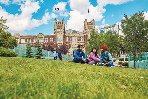 A group of SAIT students sit on the grass outside Heritage Hall in the summer.