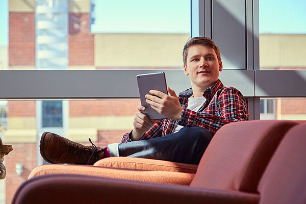 A student holds up his tablet while sitting a soft chair in the Johnson-Cobbe Energy Centre.