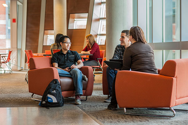 Three students sit in soft chairs in a common area in the Johnson-Cobbe Energy Centre at SAIT.