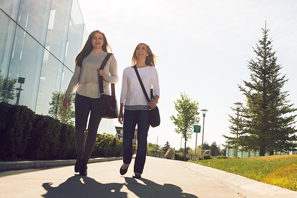 Two students walk outside SAIT's glass parking garage entrance during the summer.