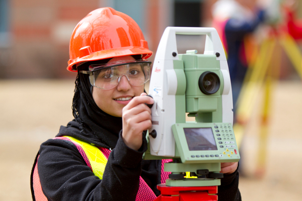 A young woman wearing a hard hat operates a GPS laser.