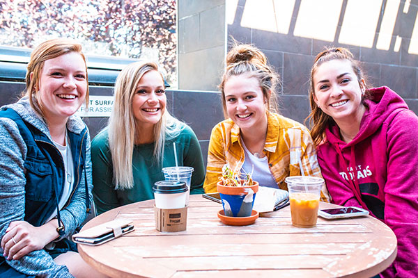 Four young women share a drink sitting on the patio of The Odyssey Coffeehouse