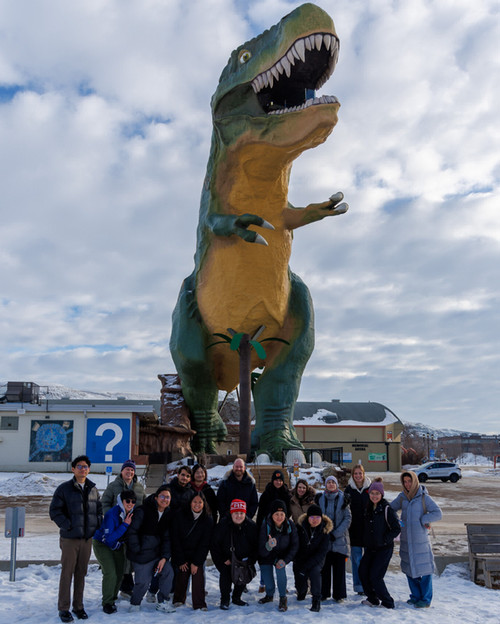 People standing in front of a dinosaur statue