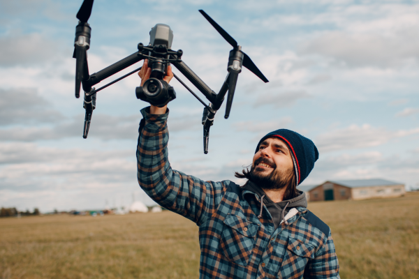 young man with facial hair holding a drone outside in field