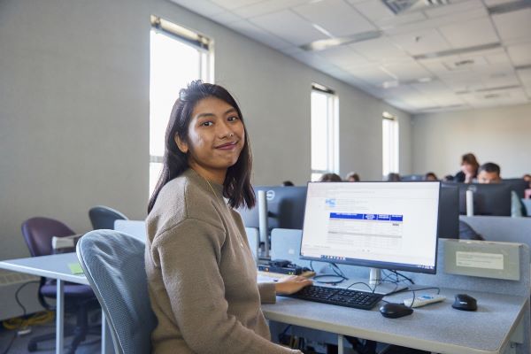 Student sitting in a computer lab and at the camera 