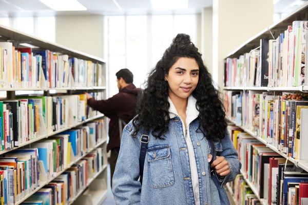 Student standing in the library while smiling at the camera