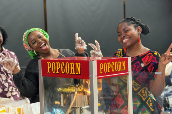 Two students smiling with their hands in peace signs, by a popcorn machine at SAIT.