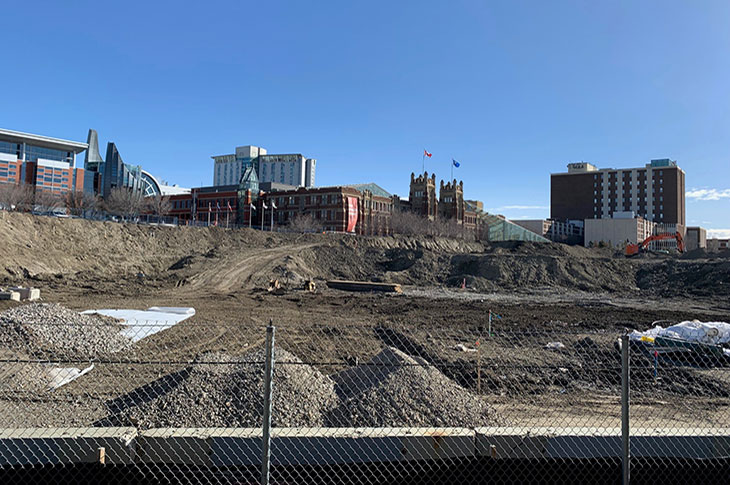 View of Campus Centre construction site from the CTrain platform. Heavy machinery moving earth and preparing the site for construction. Heritage Hall is featured in the background