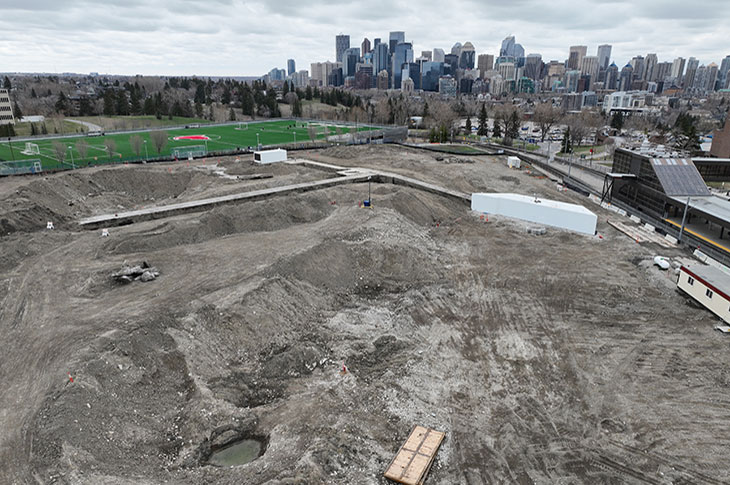 aerial view of the taylor family campus centre construction site, with a view of downtown calgary in the background