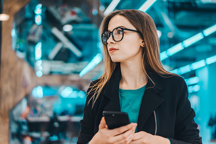 Close up image of a person holding a phone with bright lights in the background.