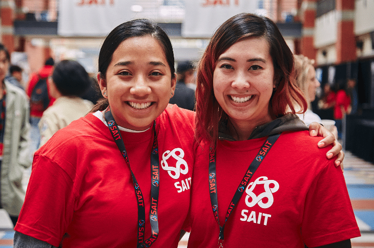 Two female volunteers in red shirts with SAIT logos smiling.