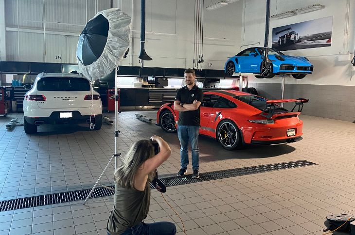 man poses for photographer with cars behind