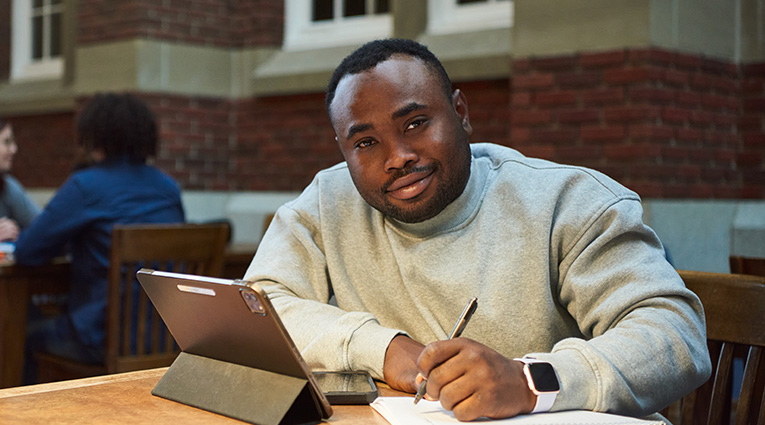 Black man in grey sweater studying and writing notes at table