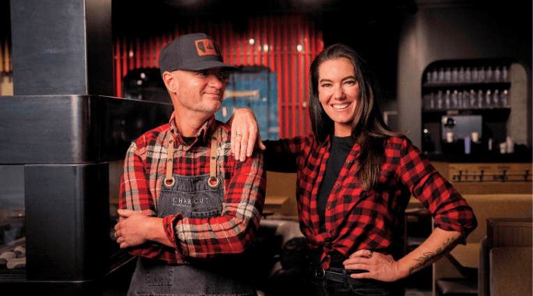 male and female chefs wearing plaid shirts and aprons smiling