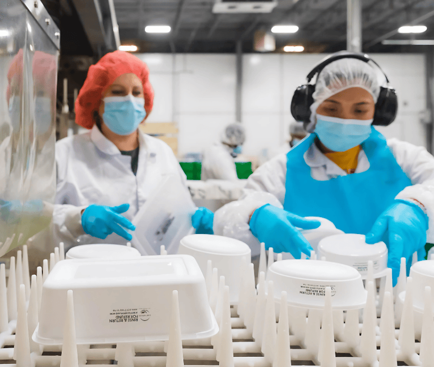 two workers stacking reusable containers on a rack