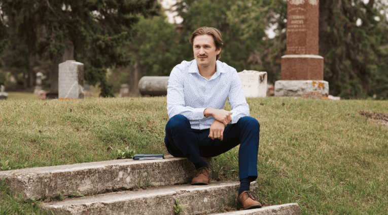 young white man sitting on steps in a graveyard