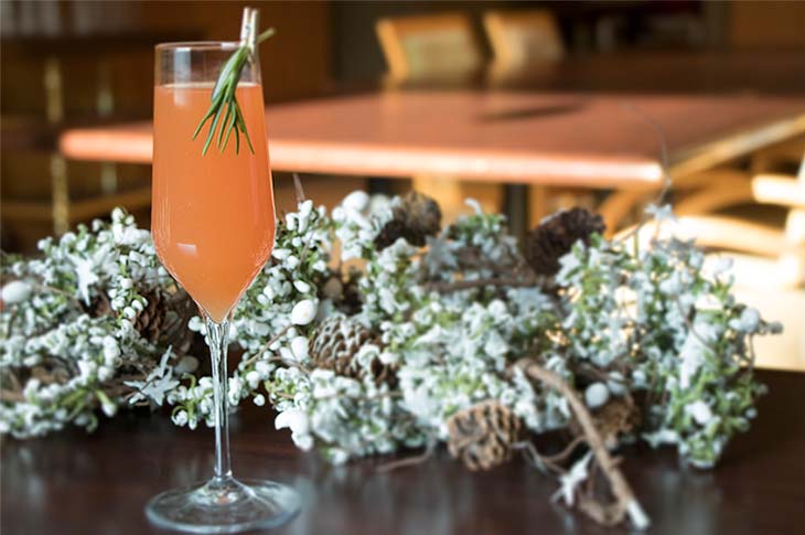 Orange Jingle Bell Swing mocktail in a champagne flute, garnished with a rosemary sprig