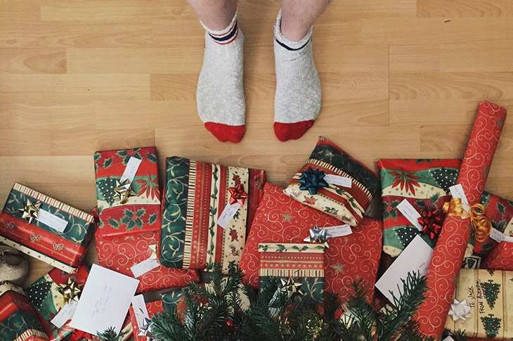 Two feet with socks on in front of Christmas presents under a tree