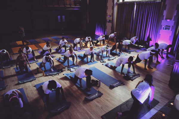 An overhead photo of a yoga class at the historic boardroom in Macdonald Hall at SAIT. The class is set in black light, so everyone is wearing white tee-shirts that glow in the dark.