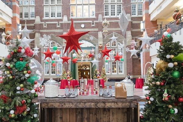 The Irene Lewis Atrium interior is decorated with many tables for guests that include large plastic domes that look like snowglobes. There are paper stars hanging from the ceiling in white, red and green. A large Christmas tree stands in the centre of the room.