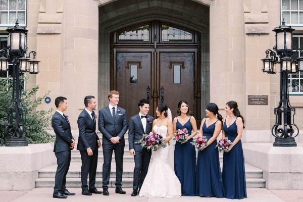 A bride and groom and their wedding party (two bridesmaids and two groomsmen) stand in front of Heritage Hall. 