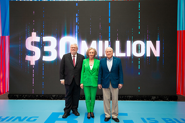 Three people pose for a photo with the text $30 million in the background