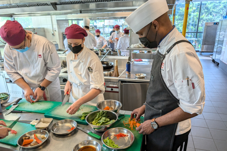 Students chop vegetables in a kitchen classroom.