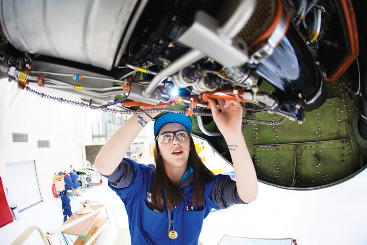 A photo of a student working on an airplane in blue coveralls.