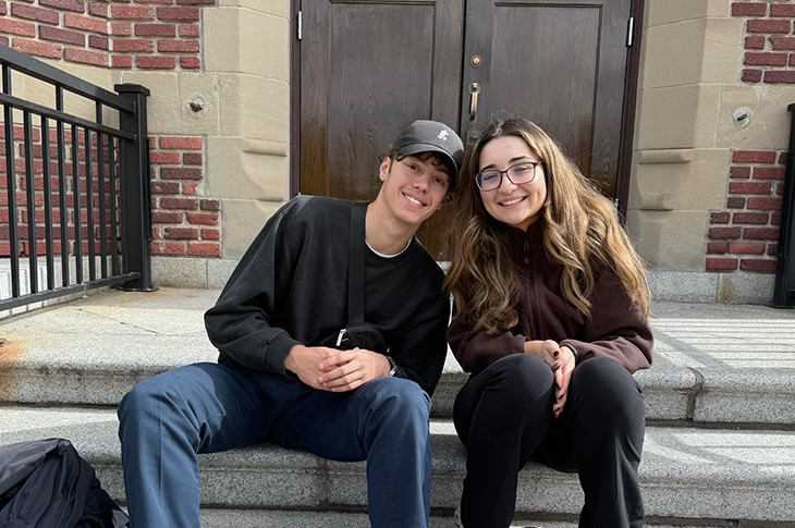 Two people pose on old stone stairs and they lean towards each other and smile for the camera.