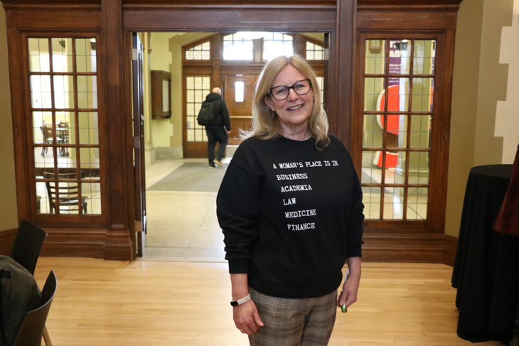 Janet Segato poses for a photo in a sweater with the text "A woman's place is in business, academia, law, medicine, finance"