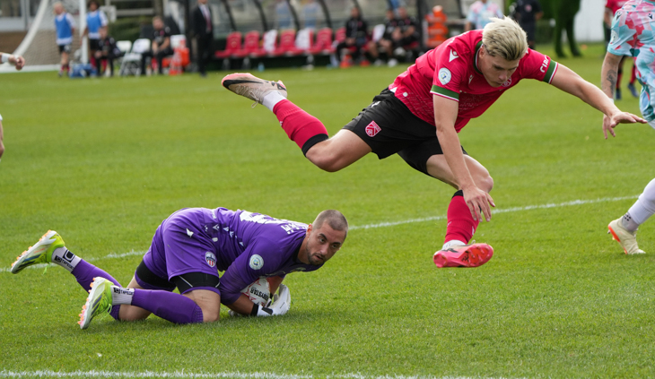 One soccer player in red is jumper over a second player in purple.