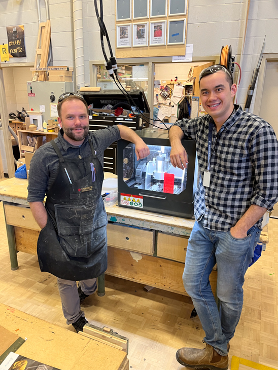 Tim and a colleague pose for a photo next to a piece of equipment