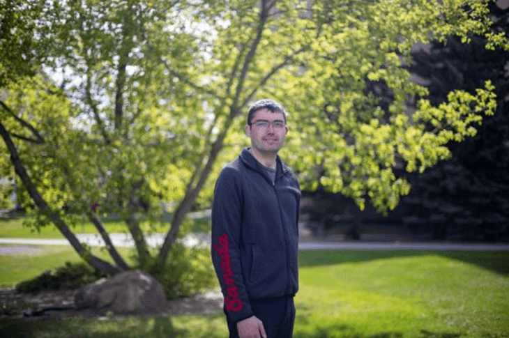 Austin Janz stands outdoors in front of a leafy tree, wearing a dark hoodie with Canada printed on the sleeve
