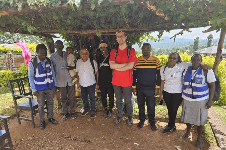 Group of individuals posing together under a vine-covered structure, showcasing teamwork and community engagement.