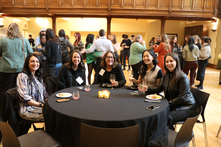 A group of five women socializing at a round table during an event.