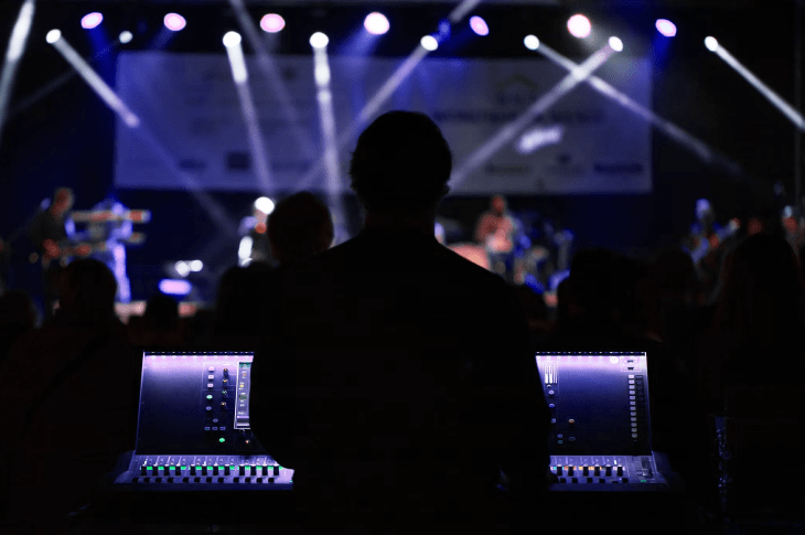 Silhouette of a sound technician managing audio controls in front of a live performance with stage lights in the background.