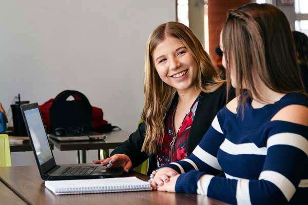 Two young women smile at one another while sitting at a table in the Johnson-Cobbe Energy Centre atrium.