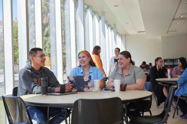 Three Indigenous students seated at a table with their laptops, smiling