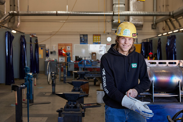 Student wearing hardhat and gloves smiles at the camera