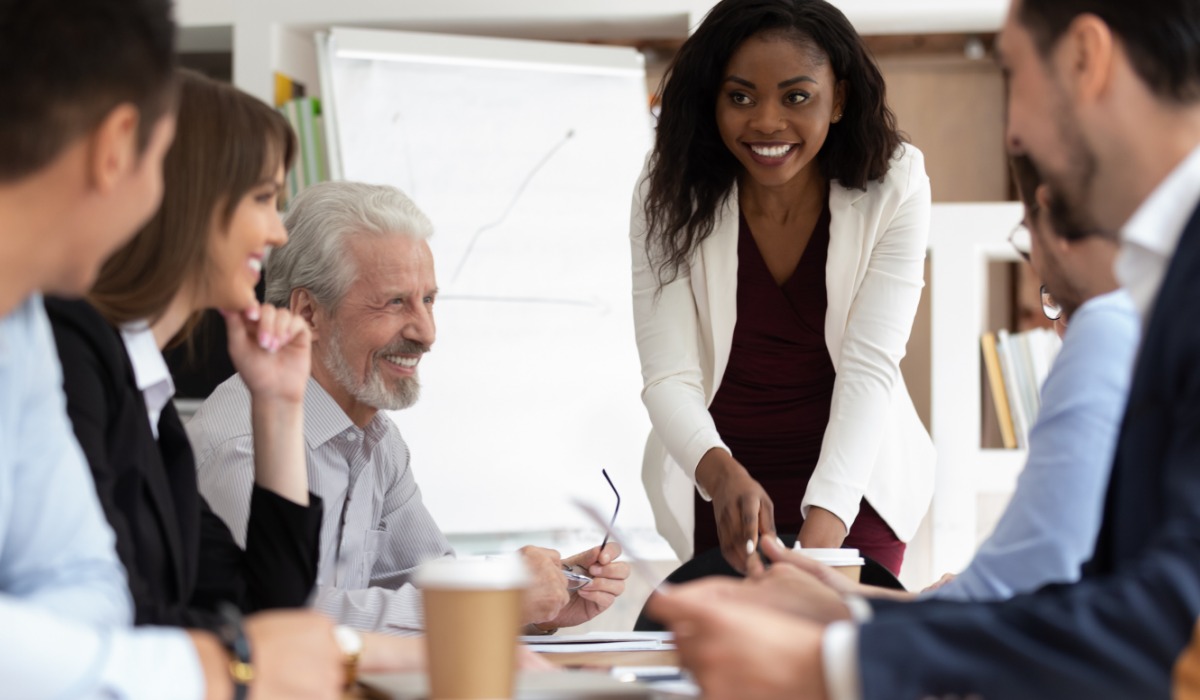 A diverse group of professionals engaging in a meeting, with a woman presenting at the forefront.